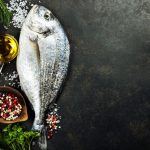 Delicious fresh fish on dark vintage background. Fish with aromatic herbs, spices and vegetables - healthy food, diet or cooking concept