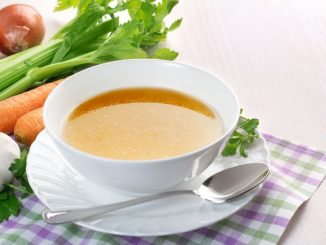 Bowl of broth (consomme) and fresh vegetables on wooden table