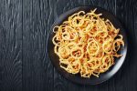french fried onions on a black plate on a black wooden table, horizontal view from above, flatlay, free space