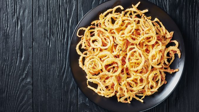 french fried onions on a black plate on a black wooden table, horizontal view from above, flatlay, free space