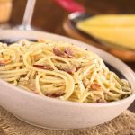 Spaghetti alla carbonara made with bacon, eggs, cheese and black pepper served in bowl with cheese to grate in the back (selective focus, focus one third into the meal)