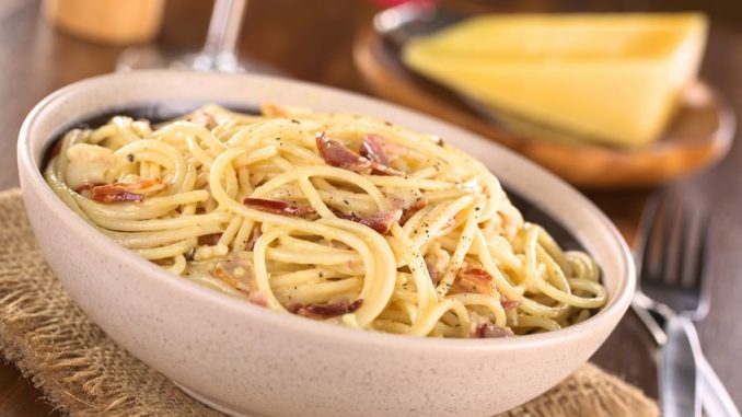 Spaghetti alla carbonara made with bacon, eggs, cheese and black pepper served in bowl with cheese to grate in the back (selective focus, focus one third into the meal)