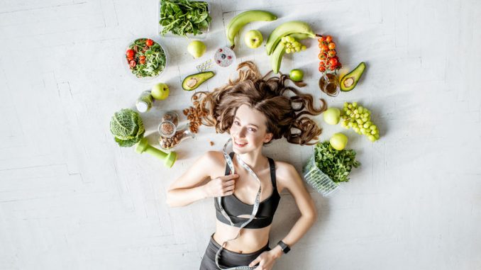 Beauty portrait of a sports woman surrounded by various healthy food lying on the floor. Healthy eating and exercise concept. Top diets 2019