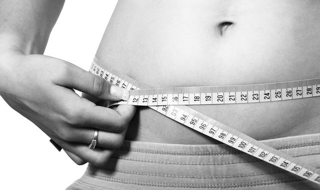 A belly with a woman measuring her waistline.. In black and white.