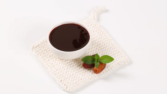 bowl of date syrup with dates on white table mat