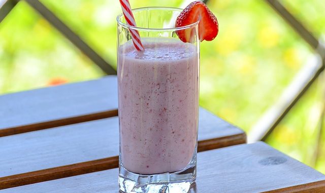 kefir strawberry smoothie in a straight glass with a strawberry garnish and straw on a wooden table.