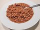 Boston-baked-beans in a white dish with spoon. Prepared with a slow cooker or multi-function cooker.