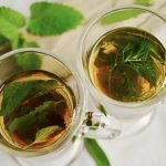 Peppermint tea leaves in two glass cups on a atble with some free green leaves.