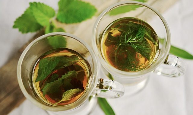 Peppermint tea leaves in two glass cups on a atble with some free green leaves.