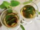 Peppermint tea leaves in two glass cups on a atble with some free green leaves.
