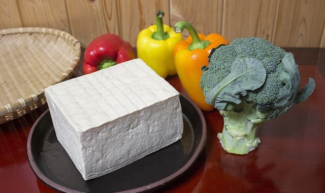 A block of tofu on a plate with peppers an broccoli as health foods.