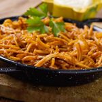Closeup of a spanish fideua, a typical noodles casserole with seafood, in a paella pan and aioli sauce in a yellow mortar on a rustic wooden table