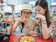two teenage chinese girls trying stinky tofu. They hold their noses.