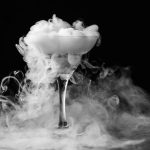 Dry ice in a champagne glass. Closeup glass with white fog at dark background. Chemical reaction of dry ice with water.