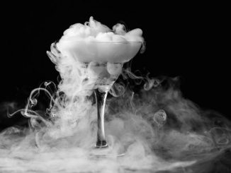 Dry ice in a champagne glass. Closeup glass with white fog at dark background. Chemical reaction of dry ice with water.