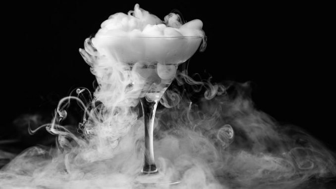 Dry ice in a champagne glass. Closeup glass with white fog at dark background. Chemical reaction of dry ice with water.