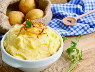 Mashed potato or puree in white bowl with crisp onions and parsley on wooden background. How to make mashed potato.