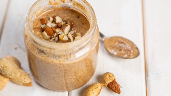 almond butter in a glass jar, white wood background