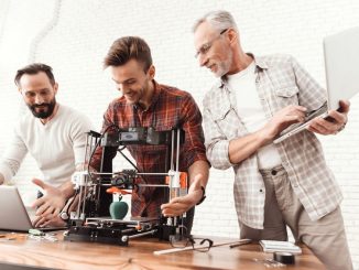 Three men are working on preparing a 3d printer for printing. Two men set up a 3d printer, an elderly man holds a laptop in his hands and watches the process. (3D Printing)