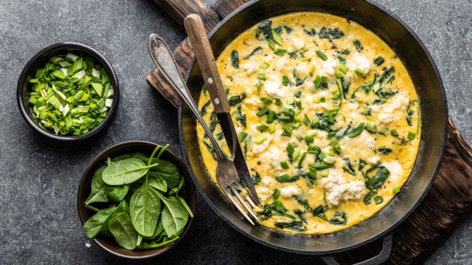 Scrambled egg omelette with spinach and cheese in a pan on the concrete background top view