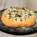 Homemade Italian rosemary, green olive and onion Focaccia bread on a baking stone.