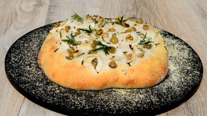 Homemade Italian rosemary, green olive and onion Focaccia bread on a baking stone.