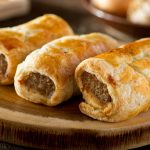 Delicious homemade sausage rolls on a wooden serving platter.