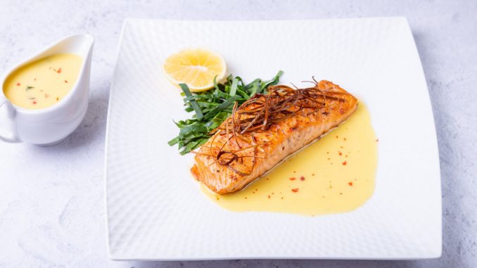 Salmon with beurre blanc sauce, spinach and lemon. Garnished with leeks. Traditional French dish. Close-up.