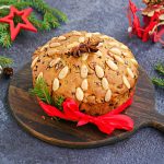 A traditional Scottish Christmas fruit Dundee cake with a mix of dried fruits, decorated with peeled almonds on a wooden board on a dark concrete background. Christmas fruitcake recipe