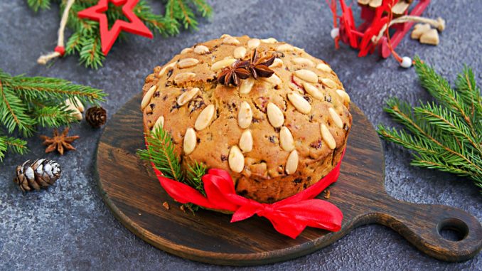 A traditional Scottish Christmas fruit Dundee cake with a mix of dried fruits, decorated with peeled almonds on a wooden board on a dark concrete background. Christmas fruitcake recipe