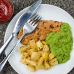 Breaded Haddock Fillet With Parmentier Potatoes And Pea Puree Against a Dark Background