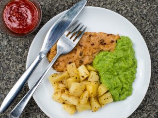 Breaded Haddock Fillet With Parmentier Potatoes And Pea Puree Against a Dark Background