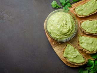 Traditional mexican homemade guacamole sauce in a glass bowl and sliced bread on a dark black stone background. Top view, copy space, horizontal image.