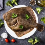 Top view of whole raw halibut fish with vegetables on black background. Omega 3 fats. Healthy for brain and mental clarity. Brain foods concept. Home cooking.
