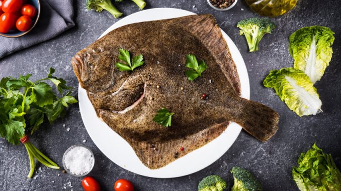 Top view of whole raw halibut fish with vegetables on black background. Omega 3 fats. Healthy for brain and mental clarity. Brain foods concept. Home cooking.