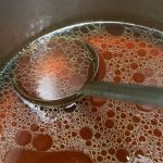 Close up shot of a pot of rich meat stock (brown stock)with a ladle.