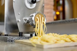 Chef cooks Italian spaghetti using a pasta machine. Pulling out long pasta in restaurant kitchen