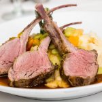 Three medium rare lamb chops taken from a rack of lambon a bed of vegetables.