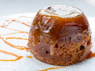 Sticky toffee pudding close up on a white sugar dusted plate drizzled with caramel sauce.