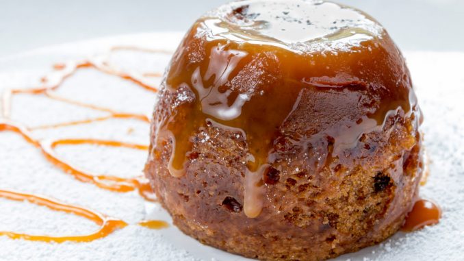 Sticky toffee pudding close up on a white sugar dusted plate drizzled with caramel sauce.