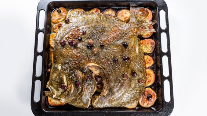 Cooked Whole Turbot fish in baking pan oven with potatoes olives and aromatic herbs isolated on white background