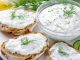 Homemade greek tzatziki sauce in a glass bowl with ingredients and sliced bread on a dark black stone background. Cucumber, lemon, dill, garlic. Close-up, horizontal image, selective focus on a bowl