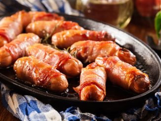Pigs in blankets. Mini sausages wrapped in smoked bacon in baking dish.
