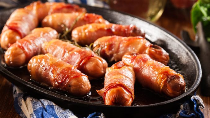 Pigs in blankets. Mini sausages wrapped in smoked bacon in baking dish.