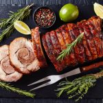 Overhead view of sliced roast pork roulade - Porchetta, delicious pork roast of Italian culinary holiday tradition on a slate tray with rosemary and lime, close-up.