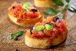 Preparing delicious Italian tomato bruschetta with chopped vegetables, herbs and oil on grilled or toasted crusty baguette sprinkled with seasoning and spices on an old grungy wooden chopping board