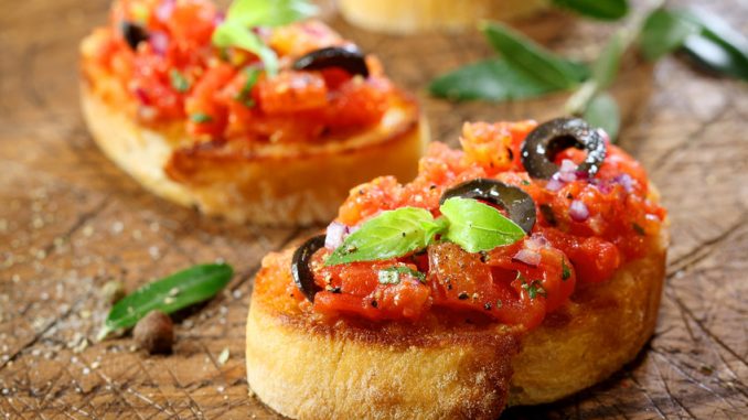 Preparing delicious Italian tomato bruschetta with chopped vegetables, herbs and oil on grilled or toasted crusty baguette sprinkled with seasoning and spices on an old grungy wooden chopping board