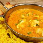 Chicken Korma a popular sweet indian curry dish of coconut and cream sauce served in a dish on a plate with pilaf rice and samosas.