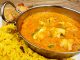 Chicken Korma a popular sweet indian curry dish of coconut and cream sauce served in a dish on a plate with pilaf rice and samosas.