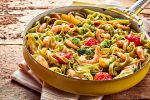 Gourmet seafood Italian tagliatelle pasta with shrimp, tomato, spinach and garlic served on a rustic wooden table in a yellow frying pan, high angle view